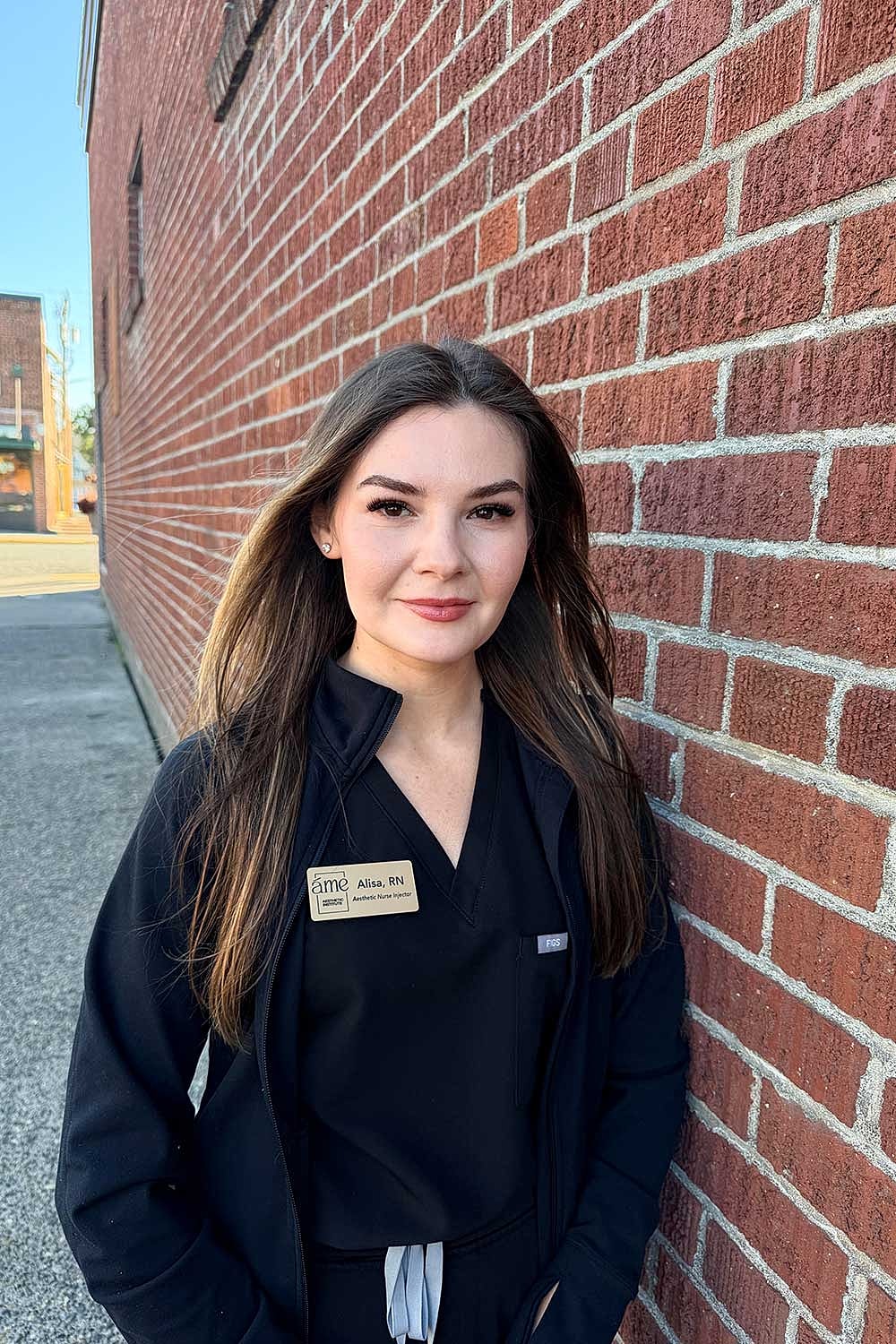 Young woman in medical attire by brick wall.