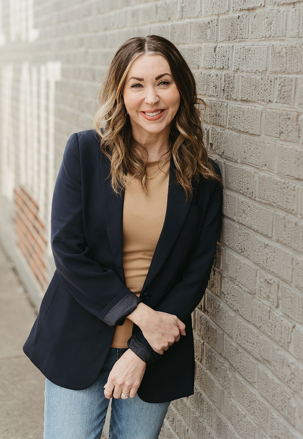 Smiling woman in blazer against a brick wall.